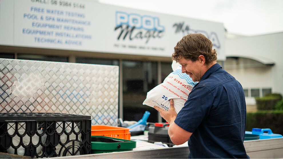 Technician unloading a bag of pool chemicals from a ute outside the pool store