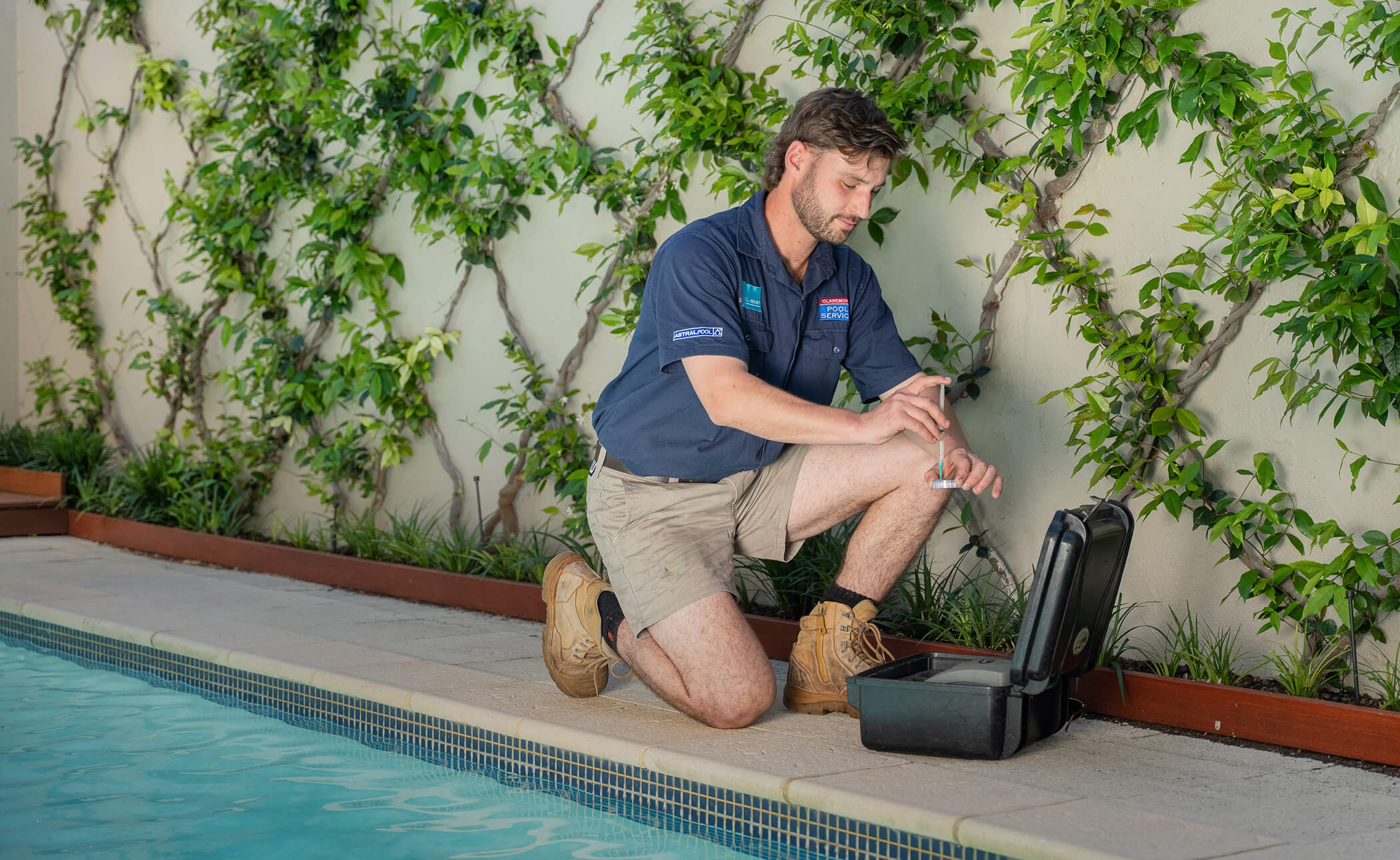 Claremont Pool Service technician kneeling at the edge of a pool with an open tool case