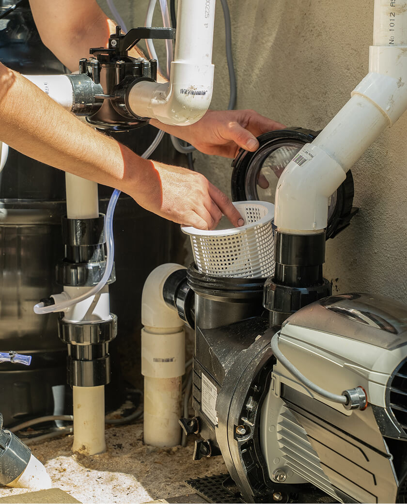 Technician removing the strainer basket from a pool pump beside the filtration plumbing